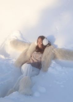 a woman sitting in the snow with her arms spread out and headphones hanging from her ears