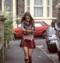 a young woman walking down a street next to parked cars