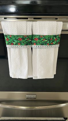 two white towels hanging from the handle of an oven door with holly and berries on them