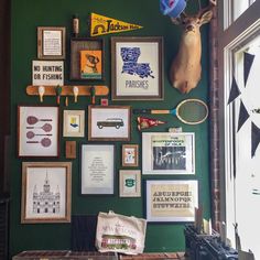 a green wall covered in framed pictures and deer head mounted to it's side