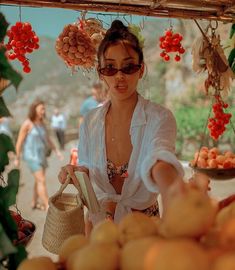 a woman in white shirt and sunglasses standing next to oranges