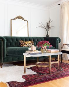 a living room with a green velvet couch and coffee table in front of a mirror