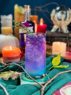 a glass filled with purple liquid sitting on top of a green blanket next to candles