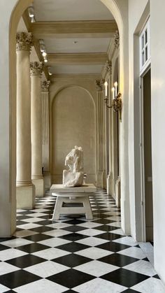 a hallway with black and white checkered flooring, columns and a marble bench