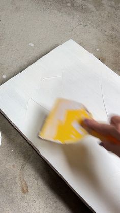 a person is painting on a piece of paper with yellow and white paint in the background