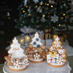 three decorated cookies sitting on top of a white plate next to a christmas tree and lit candles