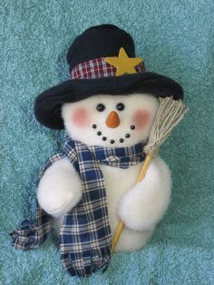 a snowman with a hat, scarf and broom laying on a blue towel in the shape of a teddy bear