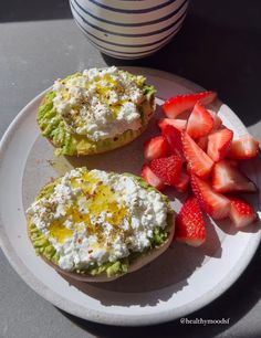 two halves of avocado and strawberries on a plate next to a cup