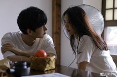 a young man and woman sitting at a table with food in front of them, looking into each other's eyes