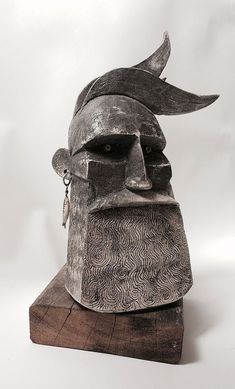 a sculpture of a man's head wearing a helmet with horns and ears on top of a piece of wood