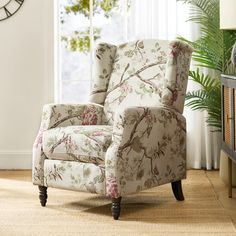 a living room with a floral chair and large clock on the wall above it's windows