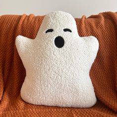 a white pillow with a ghost face on it sitting on an orange blanket in front of a wall