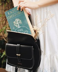 a woman is holding a book in her back pocket while wearing a white dress and black handbag