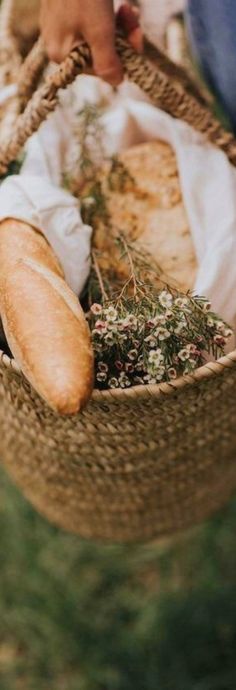 a person holding a basket with bread and herbs in it on top of the grass