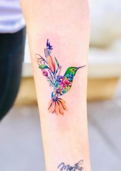 a hummingbird tattoo on the wrist with flowers and leaves around it's neck