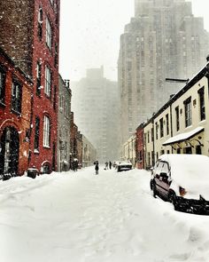 a snowy city street with cars parked on the side and people walking in the distance