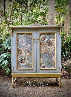 a blue cabinet with flowers painted on the doors and drawers is sitting in front of some trees