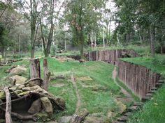 an old wooden fence in the middle of a grassy area with rocks and trees around it