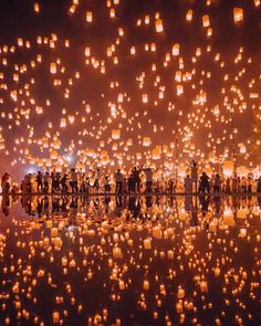 many people are gathered around floating lanterns in the air at night, with bright lights on them