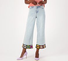 a woman wearing high rise jeans with embroidered trims and heels standing in front of a white background