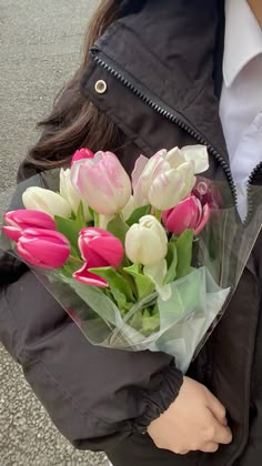 a woman holding a bouquet of pink and white tulips in her hands on the street