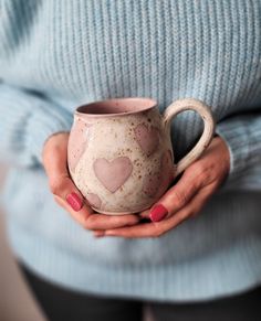 a woman holding a mug in her hands with hearts painted on the outside and inside