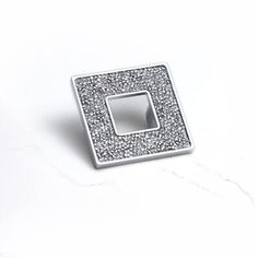 a square shaped silver ring with small sparkles in the center on a white surface