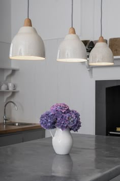 a white vase filled with purple flowers sitting on top of a kitchen counter next to a fire place