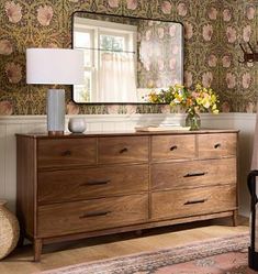 a dresser and mirror in a room with floral wallpaper on the walls behind it