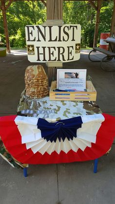 a table topped with an umbrella and books under a sign that reads, enlist here