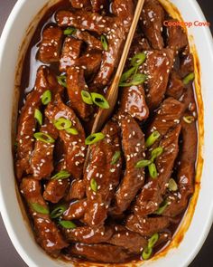 a bowl filled with meat covered in sauce and topped with green onions, sesame seeds and chopsticks