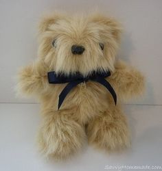 a teddy bear with a blue ribbon around it's neck sitting on a white surface