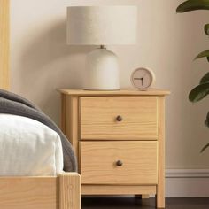 a nightstand with a clock on top of it next to a bed and potted plant