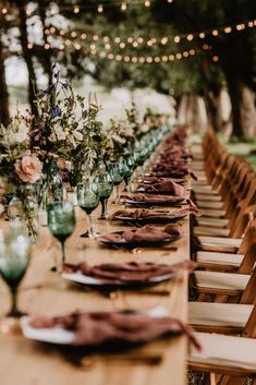 a long table set up with place settings and flowers on it for an outdoor dinner