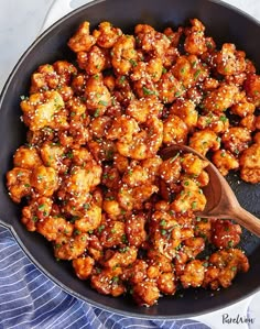 a skillet filled with chicken covered in sesame seeds and teriyaki sauce next to a wooden spoon