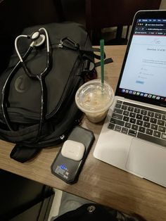 an open laptop computer sitting on top of a wooden desk next to a bag and cell phone