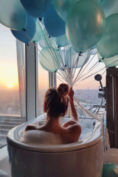 a woman in a hot tub with balloons floating over her head and the sun shining through the window