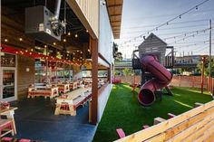 an outdoor dining area with tables, benches and a slide in the back ground is lit by string lights