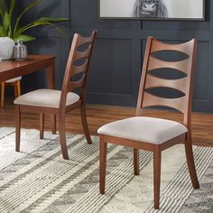 two wooden chairs sitting on top of a rug next to a table and chair in front of a painting