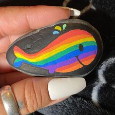 someone is holding a painted rock with a rainbow whale on it