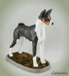 a figurine of a dog standing on top of a moss covered base with white and brown spots