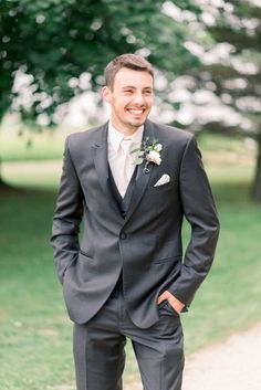 a man in a suit and tie standing on a dirt road smiling at the camera