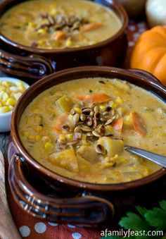 two brown bowls filled with soup next to corn and carrots on top of a table