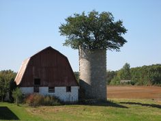 an old barn and silo stand in the middle of a field with trees growing out of it