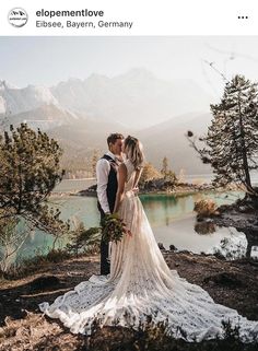 a bride and groom standing next to each other in front of a lake surrounded by mountains