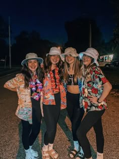 three girls are standing in the street at night wearing sun hats and flowered shirts