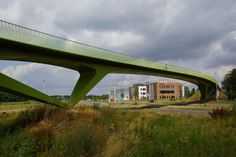 a green bridge over a road with buildings in the back ground and clouds in the sky