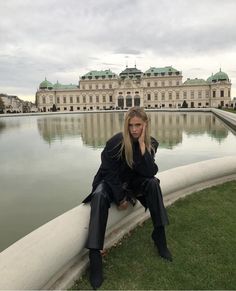 a woman sitting on the edge of a pond in front of a large building