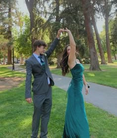 a young man and woman dressed in formal wear standing on grass with trees behind them