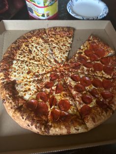 a pepperoni pizza sitting in a box on a table next to a cup and sauce